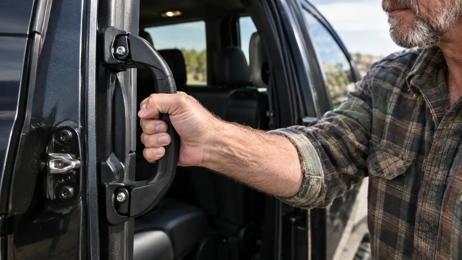 A hand gripping a portable car handle that is anchored in the SUV door latch, with the door open