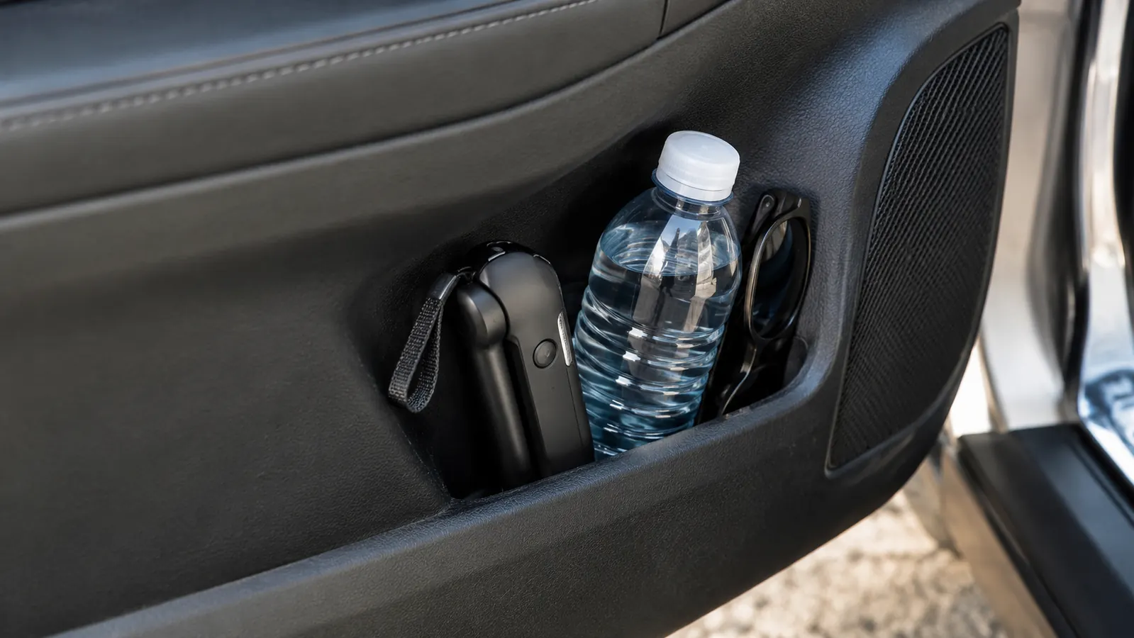 A portable car handle resting in a car door pocket beside a water bottle and sunglasses